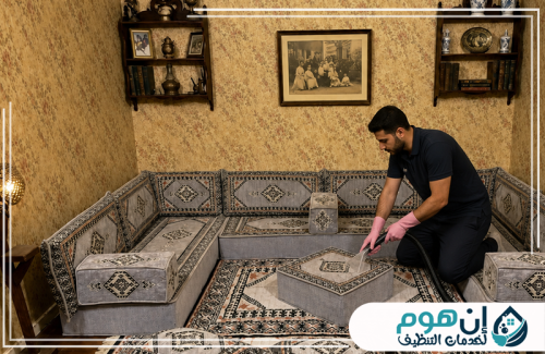 تنظيف كنب وسجاد بالبخار بجدة 0559016158 شركة إين هوم للتنظيف عامل ينظف مجلسًا عربيًا أرضيًا باستخدام جهاز شفط لإزالة الغبار والبقع من القماش.