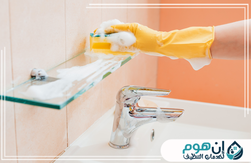 تنظيف دورات المياه بجدة 0559016158 شركة إين هوم للتنظيف تنظيف الرف الزجاجي في الحمام باستخدام إسفنجة ومنظف رغوي لإزالة البقع.